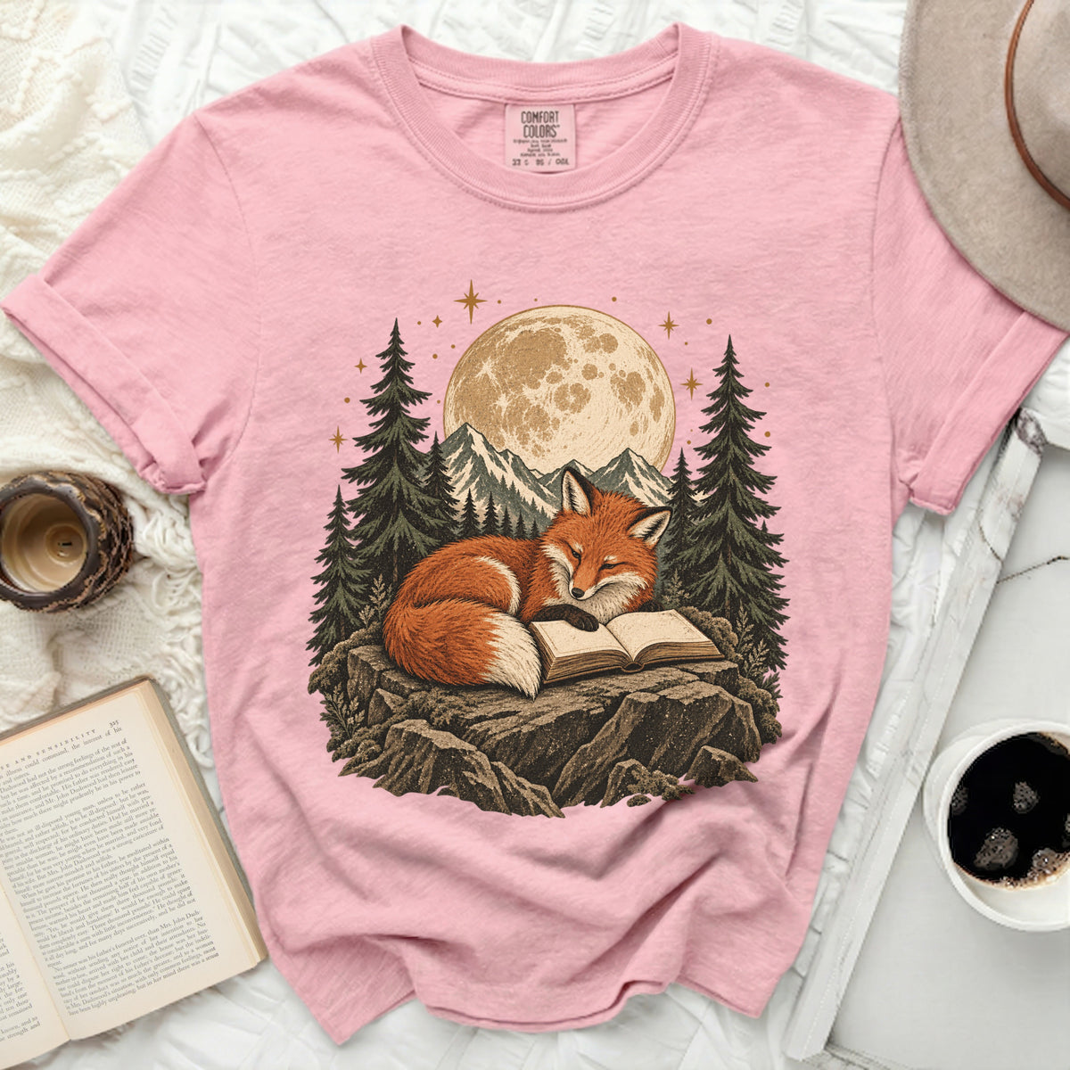 Pink t-shirt with a graphic of a fox reading a book under a moonlit sky.