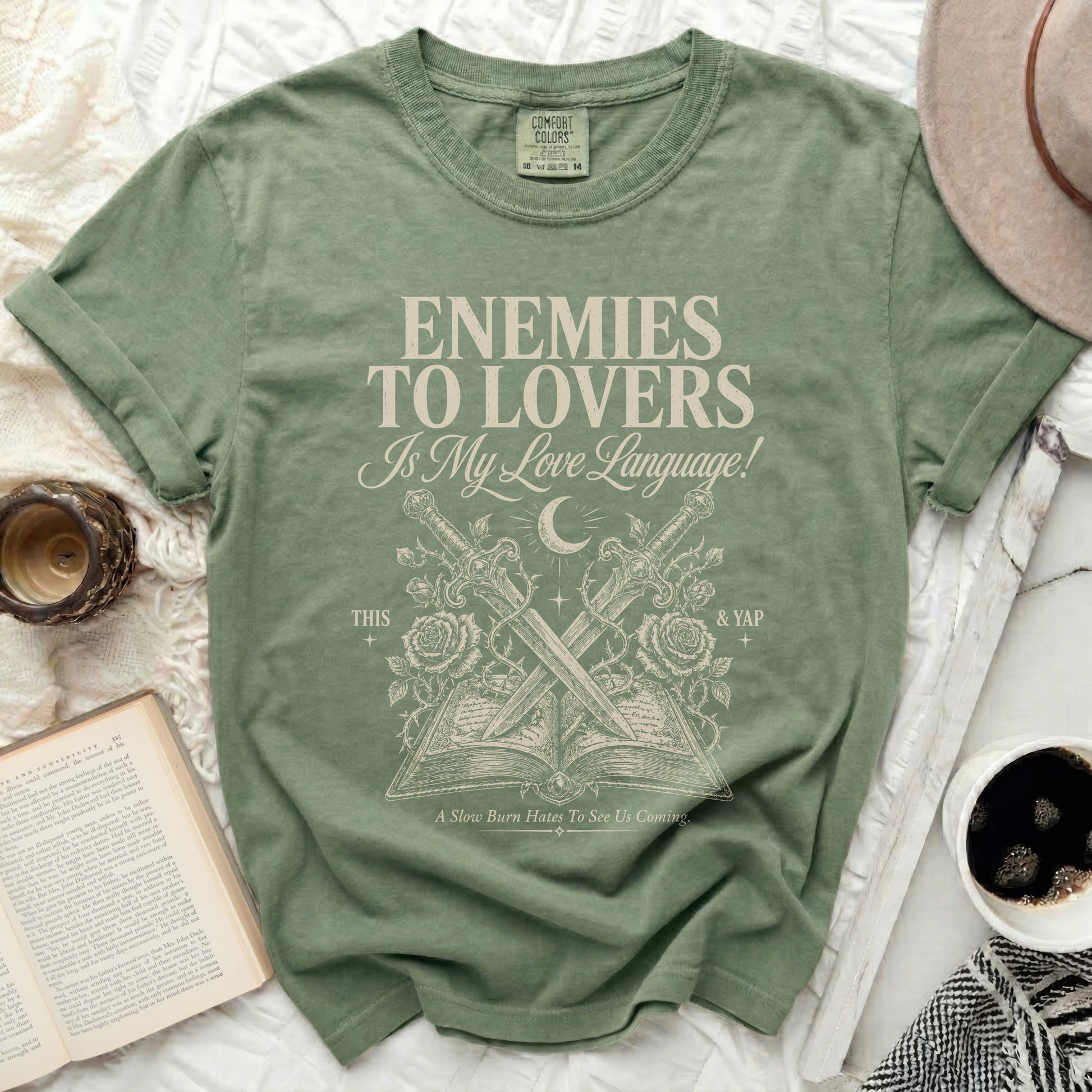 Green t-shirt with "Enemies to Lovers" text, crossed swords, and open book graphic.