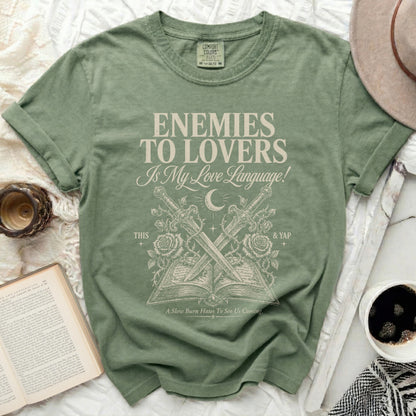 Green t-shirt with "Enemies to Lovers" text, crossed swords, and open book graphic.