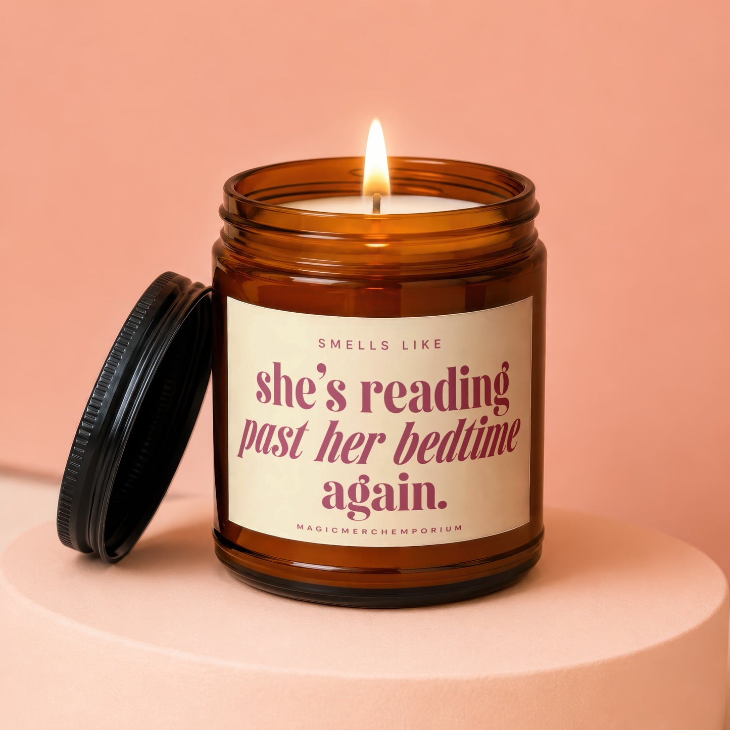 Candle in amber jar with lid off, lit flame, text "Smells like she's reading past her bedtime again."