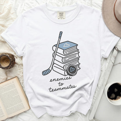 White t-shirt with stacked books, hockey stick, and puck, reading "enemies to teammates."