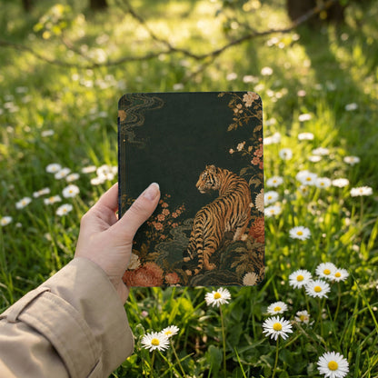 Notebook with tiger and floral design held in hand amid daisies.