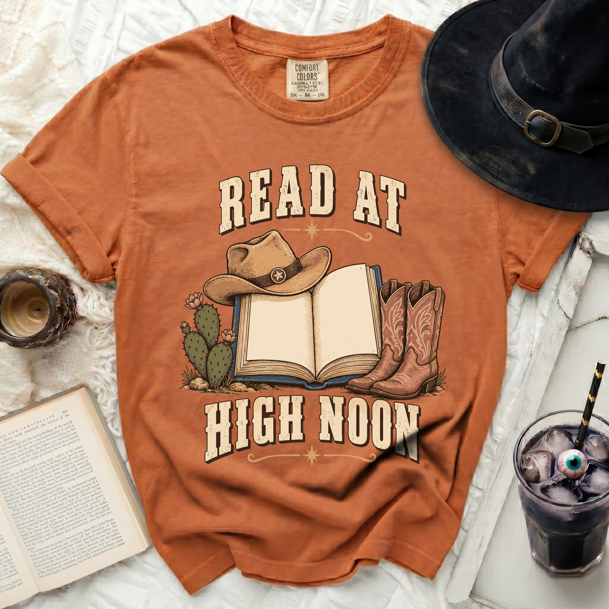 T-shirt with cowboy hat, boots, cacti, and open book reading "READ AT HIGH NOON".
