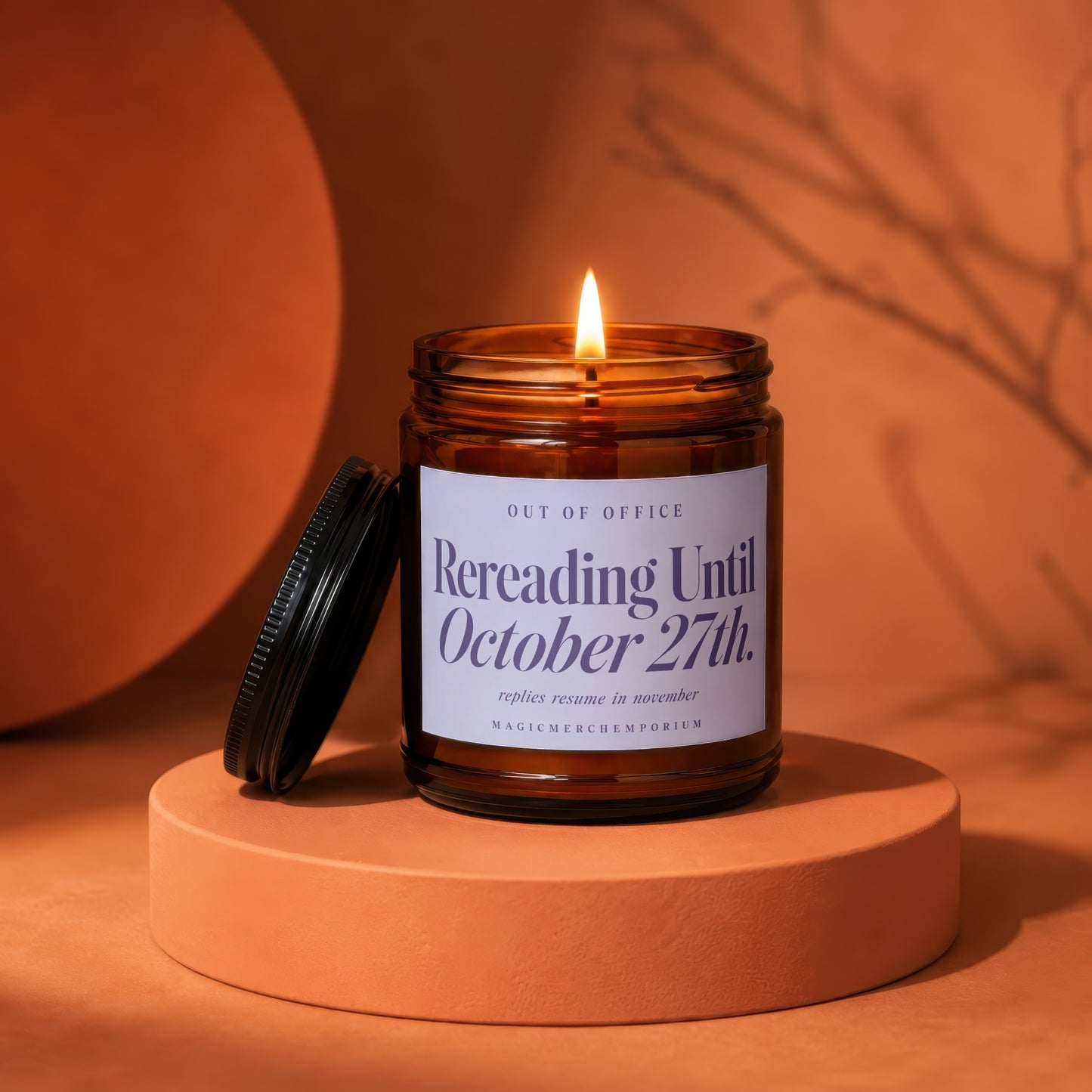 A burning candle in an amber jar rests on an orange pedestal, with its black lid leaned beside it against a warm, monochrome background.