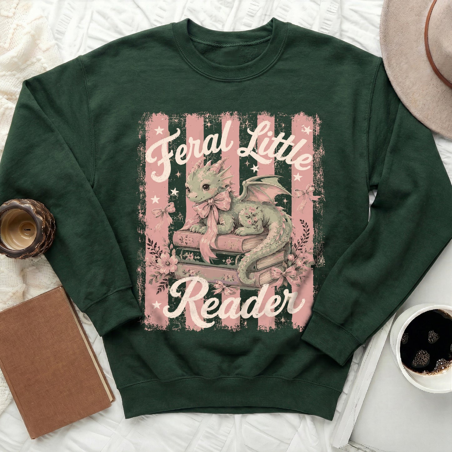 Dark green sweatshirt with a pastel dragon on stacked books graphic that reads "Feral Little Reader".