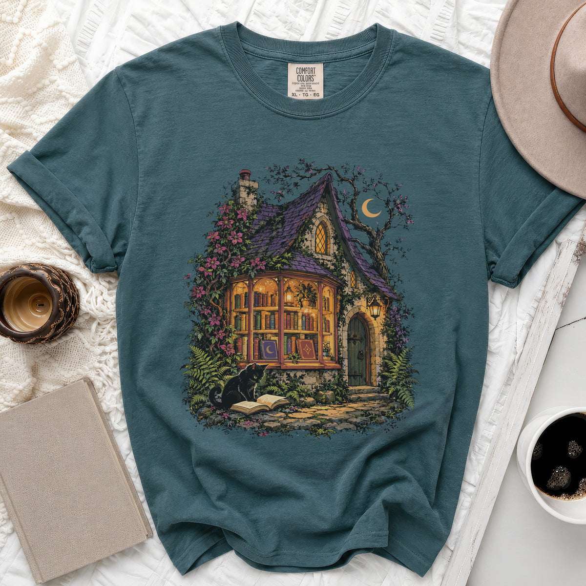 Teal Comfort Colors t-shirt with a whimsical cottage scene, black cat, and books.