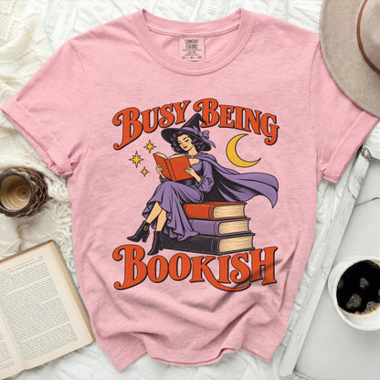 Pink t-shirt with graphic of witch reading book and text "Busy Being Bookish".