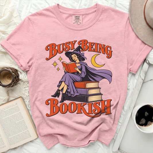 Pink t-shirt with graphic of witch reading book and text "Busy Being Bookish".