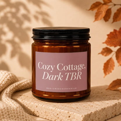 Amber candle with pink label reading "Cozy Cottage, Dark TBR".