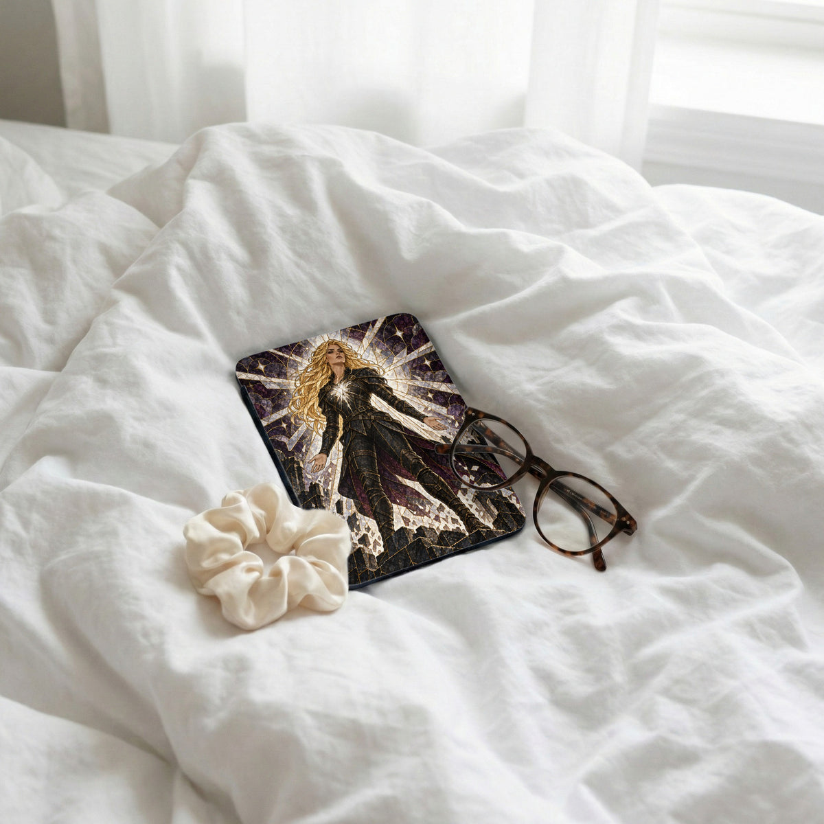 Book with stained glass woman, scrunchie, and glasses on white sheets