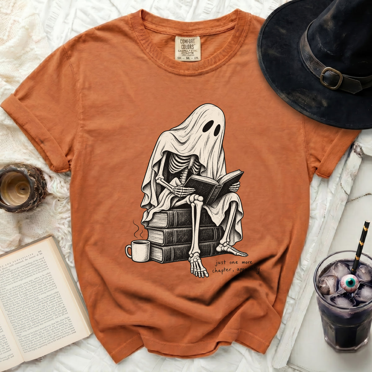 Skeleton ghost reading a book on a stack of books with text "just one more chapter, apparently".