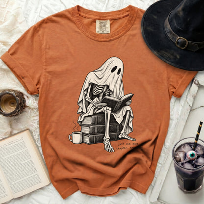Skeleton ghost reading a book on a stack of books with text "just one more chapter, apparently".