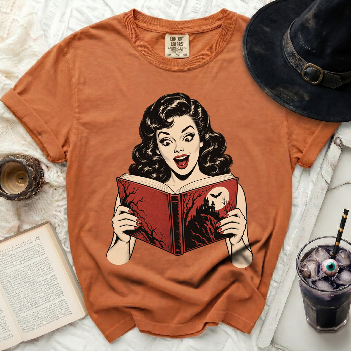 Orange t-shirt with a retro comic graphic of a surprised woman reading a spooky book.