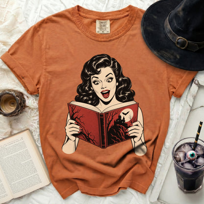 Orange t-shirt with a retro comic graphic of a surprised woman reading a spooky book.