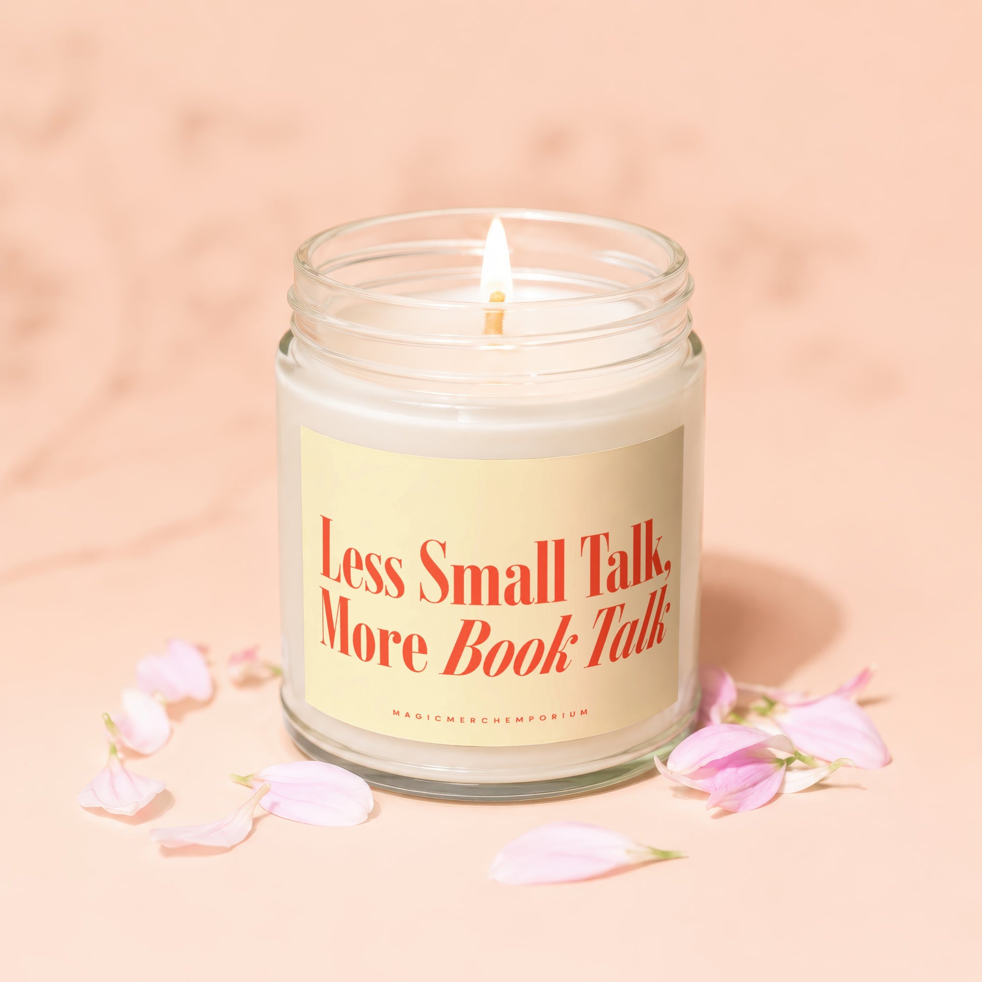 Glass jar candle with lit wick on a pink background with flower petals.