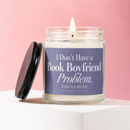 A lit candle in a clear glass jar with a black lid on a white pedestal, featuring a purple label with the white text "I Don't Have a Book Boyfriend Problem. Azriel is a lifestyle." against a pink background.