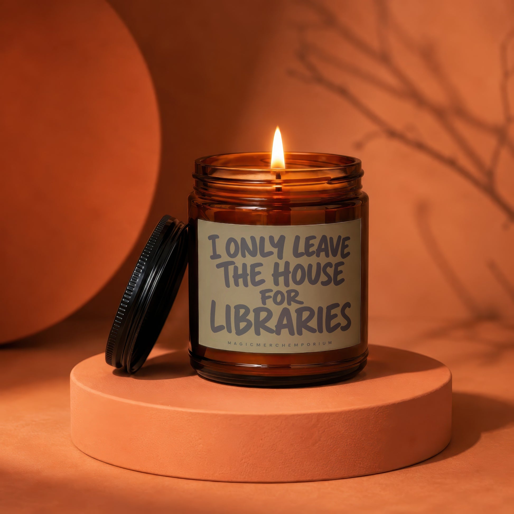 Amber glass candle with burning wick and text "I only leave the house for libraries".