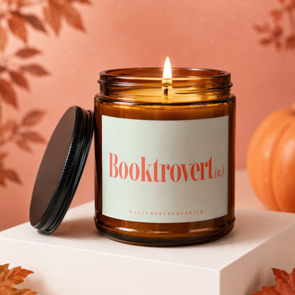 Amber jar candle with "Booktrovert (n.)" label, lit flame, and autumn decor.