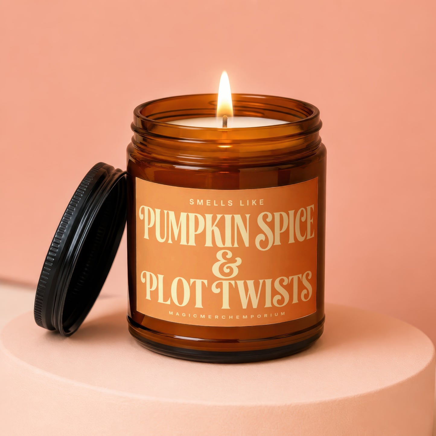 Amber jar candle with lit flame, lid off. Text reads: Smells like Pumpkin Spice & Plot Twists.