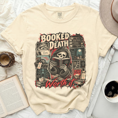 Cream t-shirt graphic featuring grim reaper reading with text "Booked to Death Worth It."