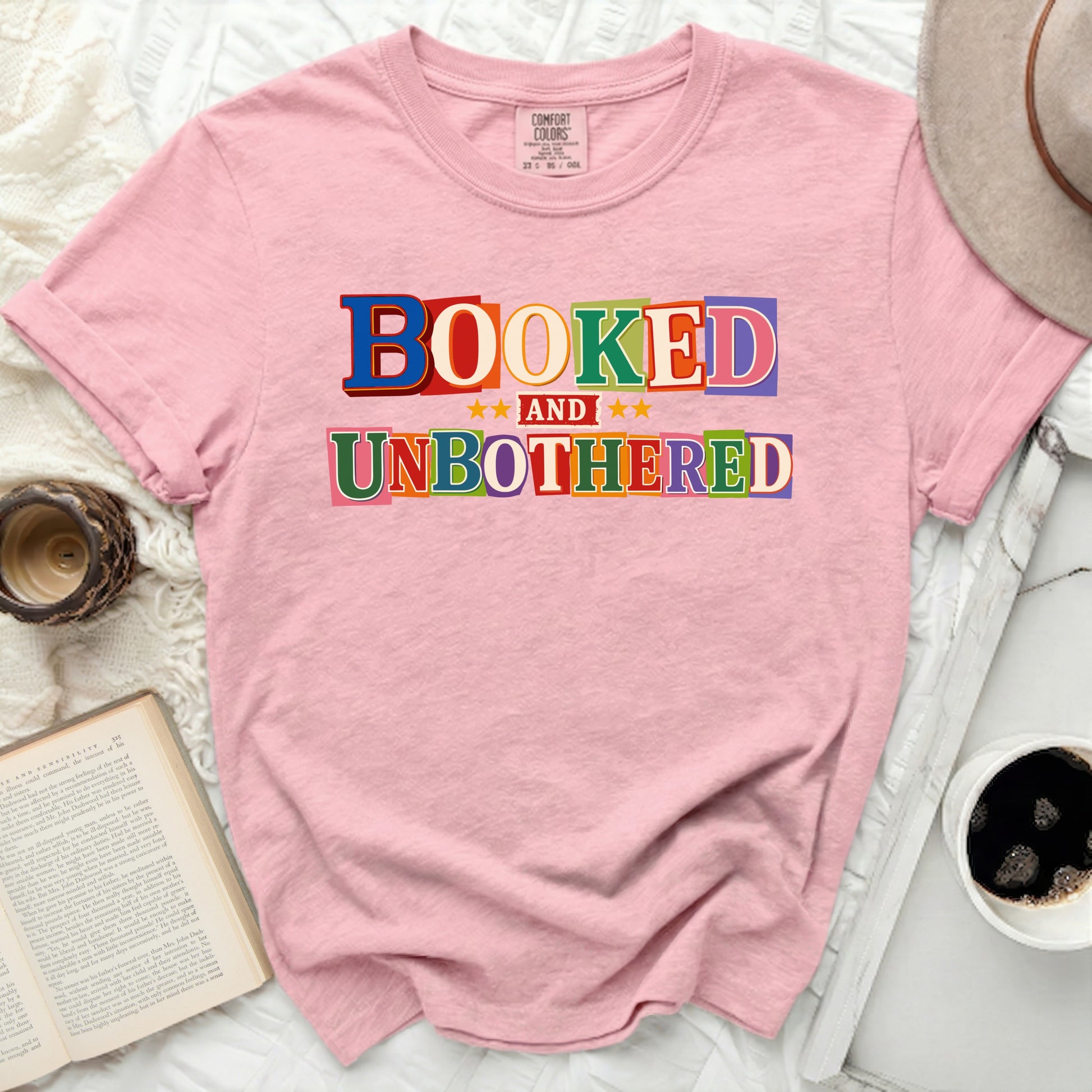 "Booked And Unbothered" graphic tee on a pink shirt.