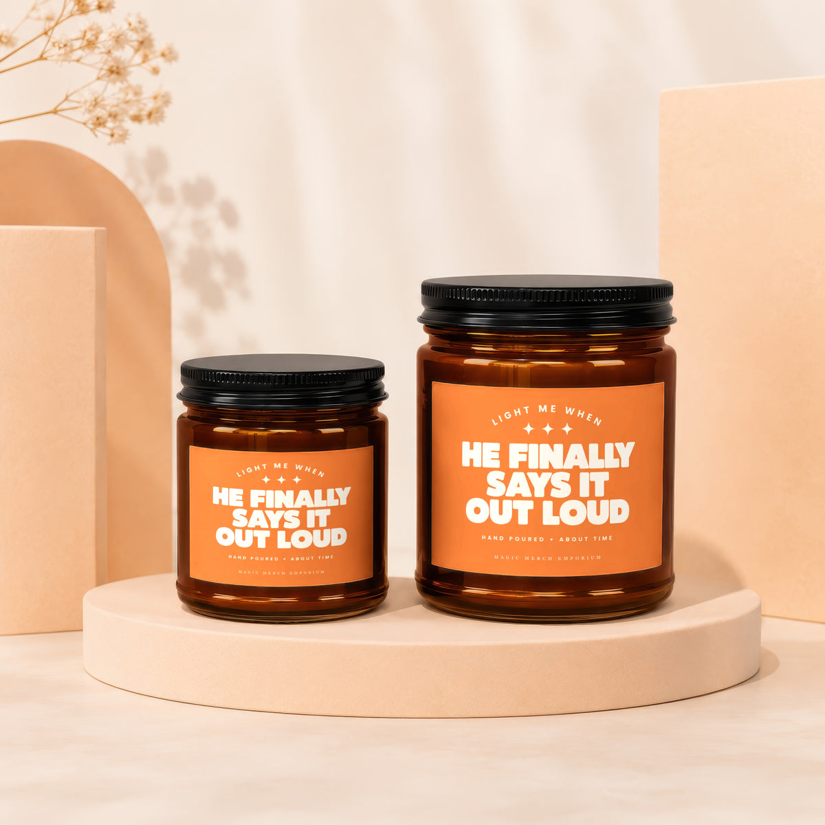 Two amber jar candles with black lids and orange labels reading "He finally says it out loud".