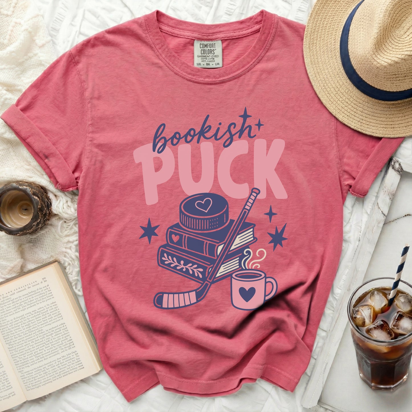 Pink t-shirt with "bookish+ PUCK" text, hockey stick, books, and mug.