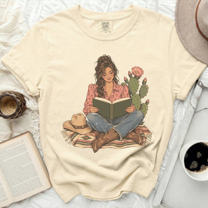 Comfort Colors t-shirt with illustration of woman reading by cactus and cowboy hat.