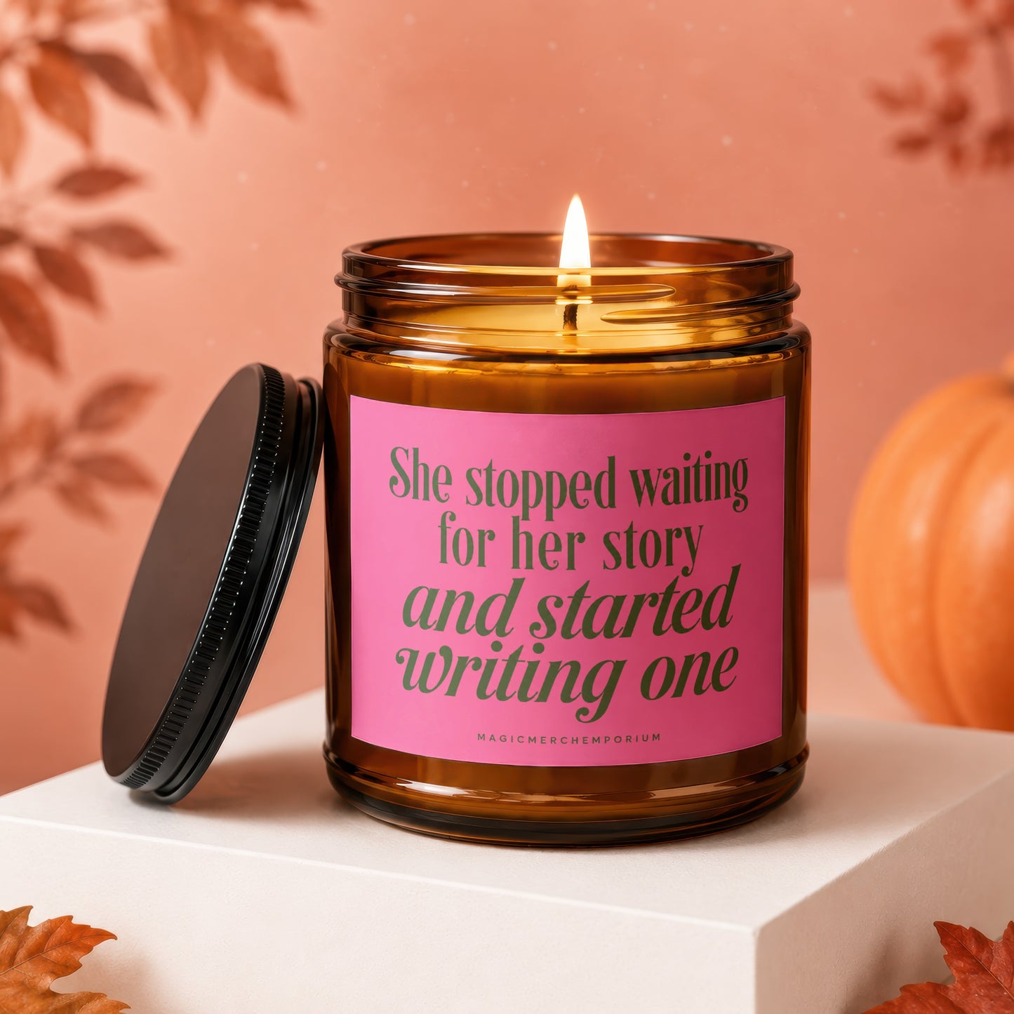Amber candle with pink label reading "She stopped waiting for her story and started writing one".