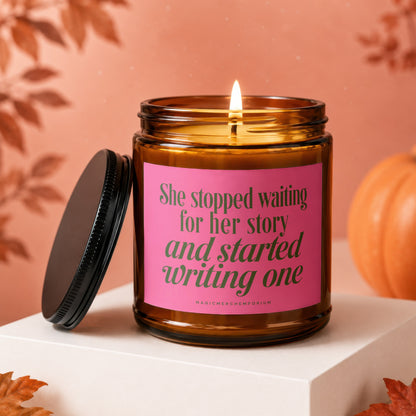 Amber candle with pink label reading "She stopped waiting for her story and started writing one".