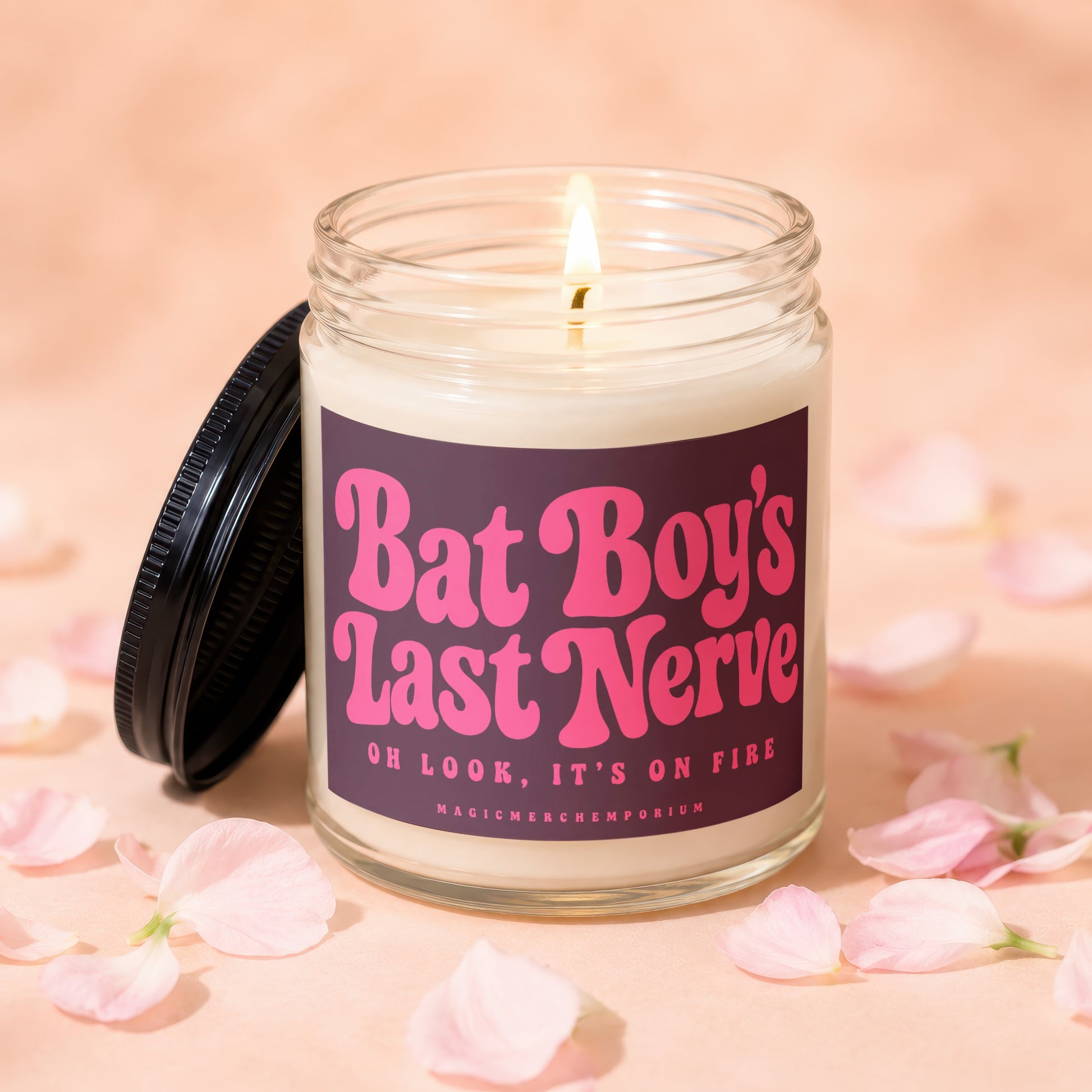 Lit candle in a glass jar with a black lid, featuring pink text "Bat Boy's Last Nerve. Oh Look, It's On Fire."