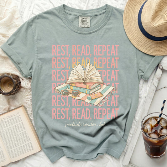 Green t-shirt with "REST, READ, REPEAT" repeating and a book on a striped blanket.