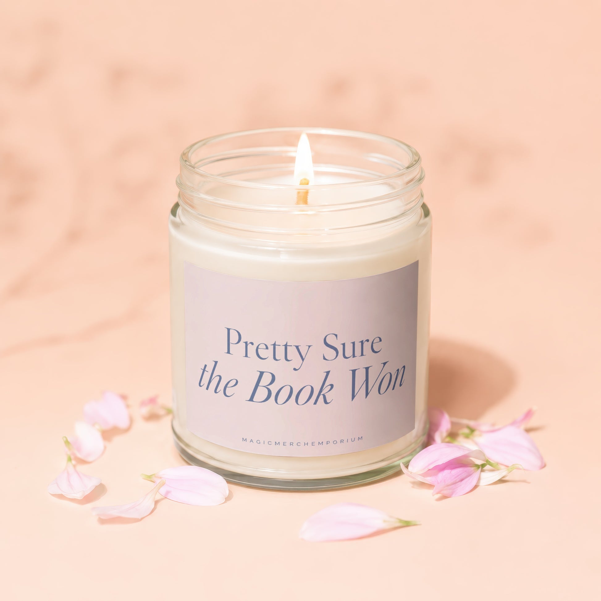 Candle with lit flame and "Pretty Sure the Book Won" text on label.