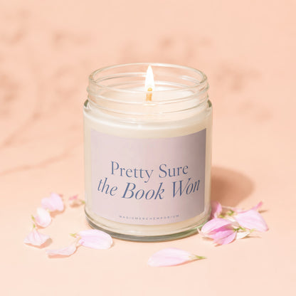 Candle with lit flame and "Pretty Sure the Book Won" text on label.