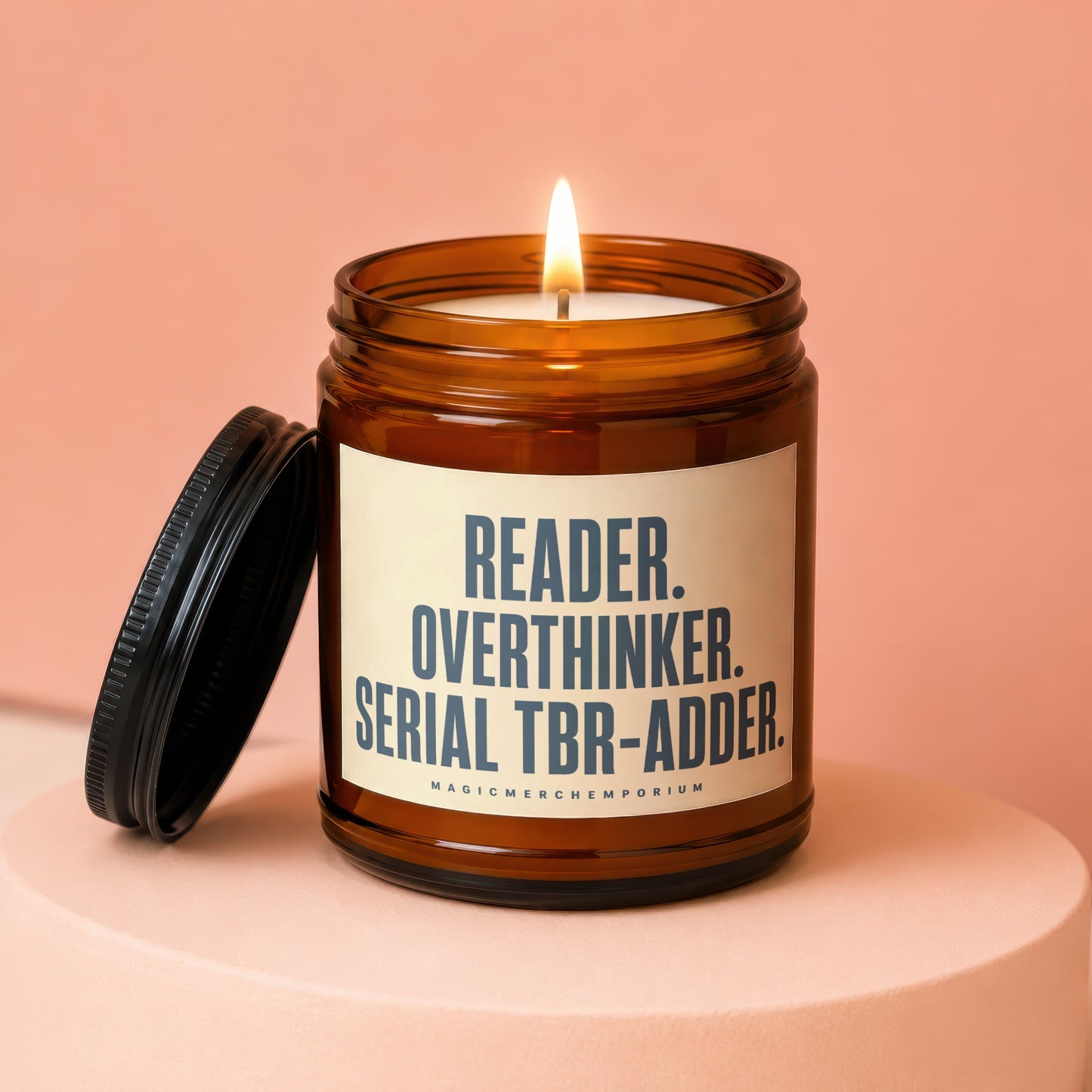 Amber candle with lit wick and lid off, featuring text "READER. OVERTHINKER. SERIAL TBR-ADDER."