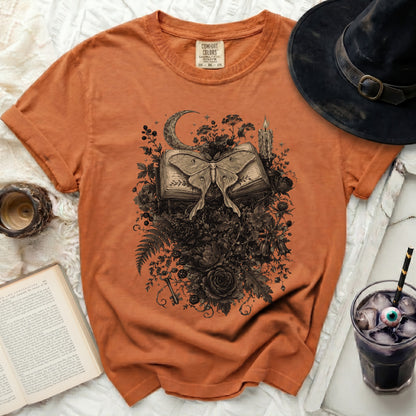 Orange t-shirt with moth, open book, moon, and floral graphic.