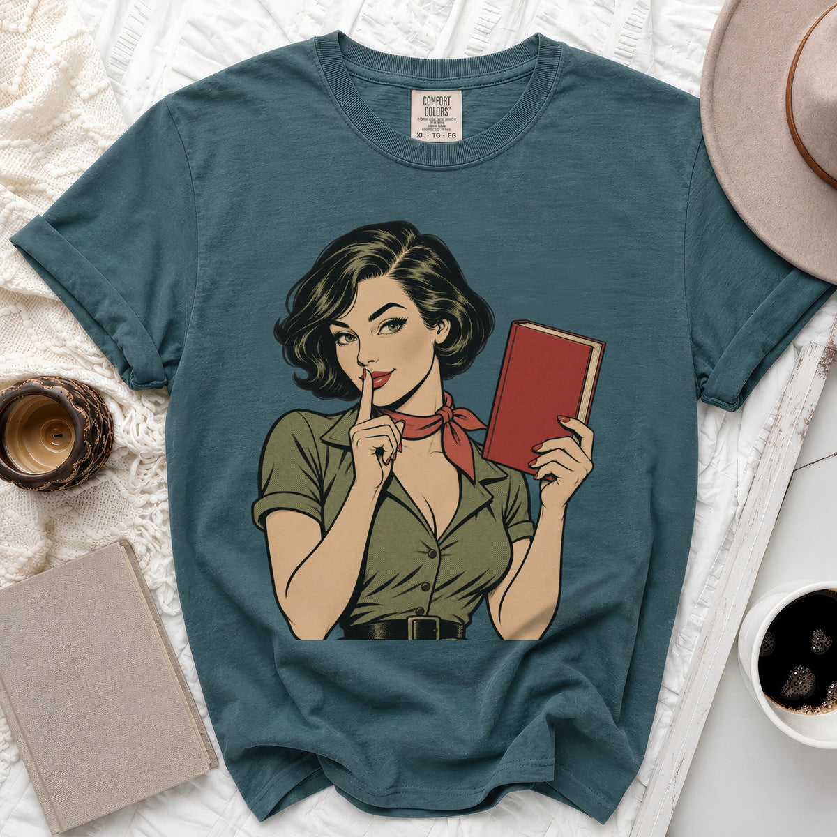 Comic book style graphic of woman holding book and gesturing for quiet on teal t-shirt.