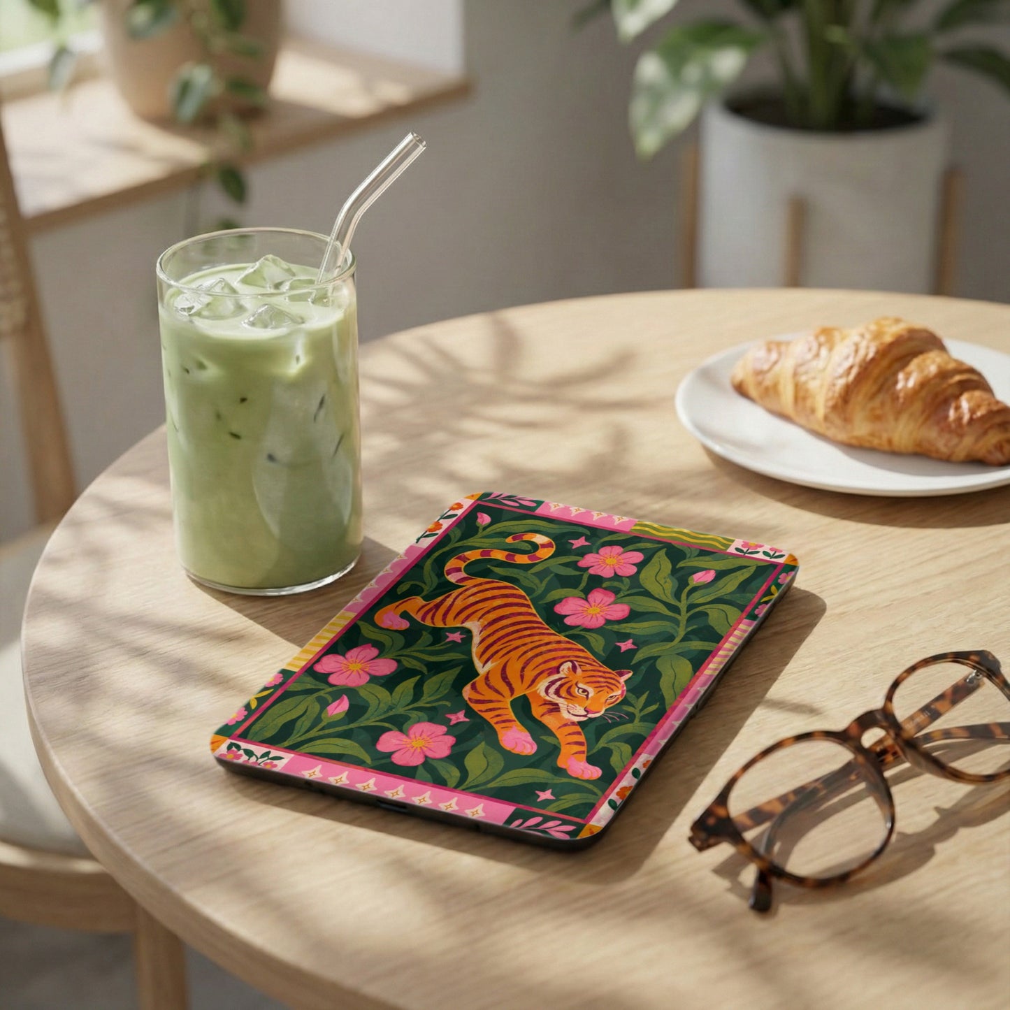 Coaster with orange tiger on dark green floral background next to matcha latte and croissant.