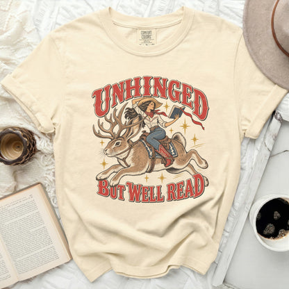 Cream t-shirt graphic with text "Unhinged but well read" featuring a woman riding a jackalope.