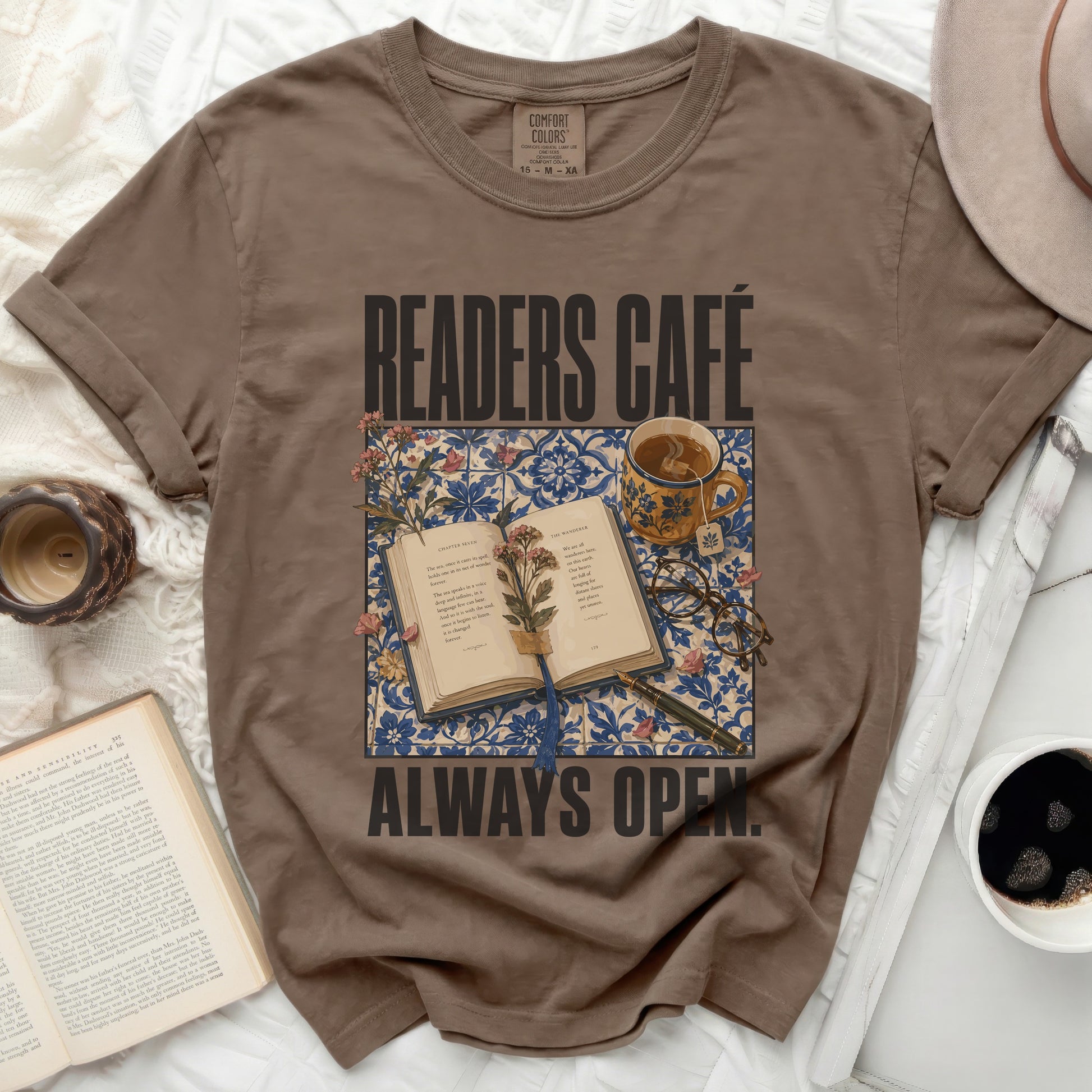 Brown t-shirt with "Readers Café Always Open" text and floral book illustration.