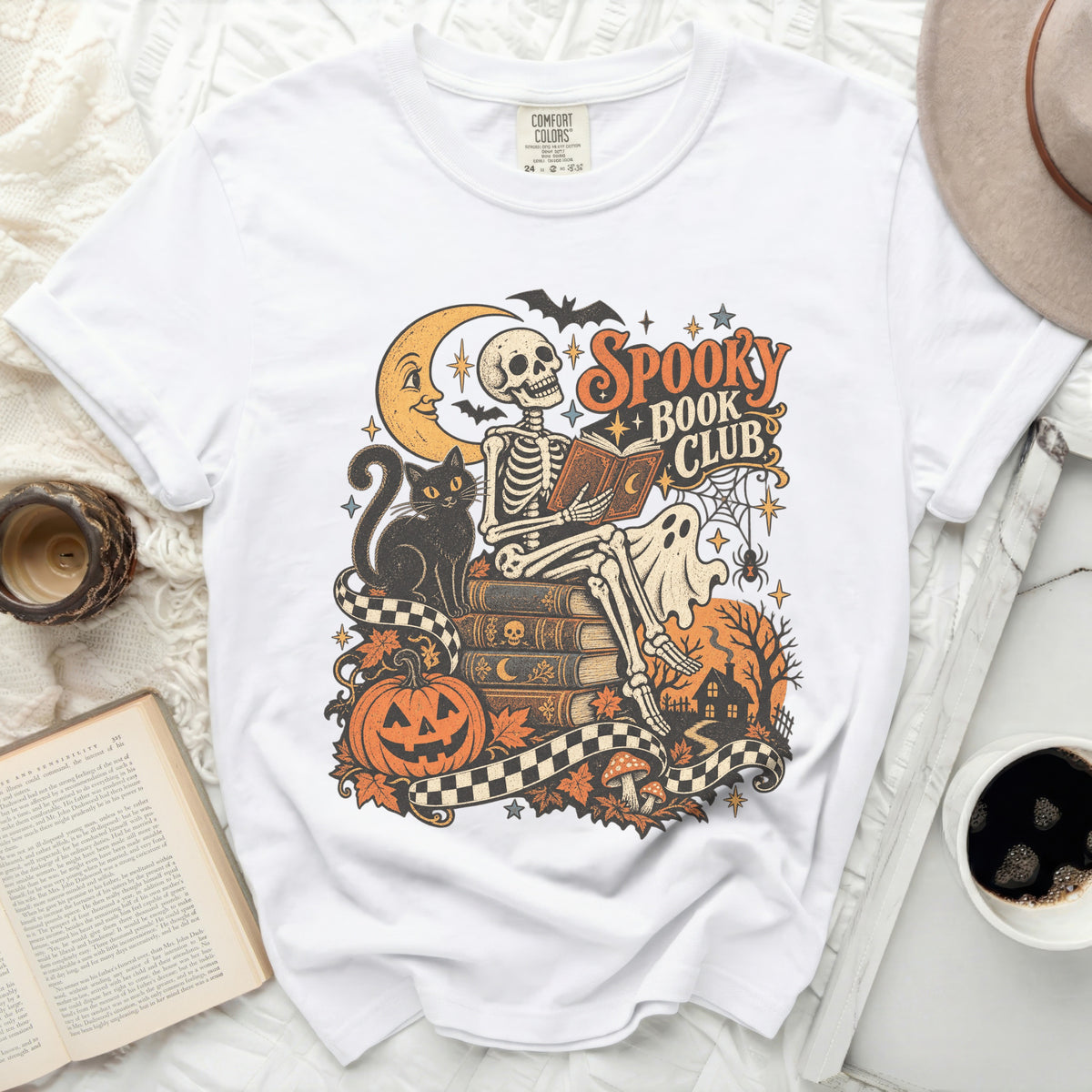 White t-shirt with "Spooky Book Club" Halloween graphic featuring a skeleton reading.