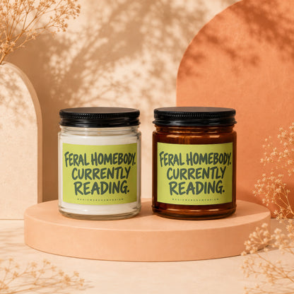 Two candles with "Feral Homebody. Currently Reading." text, one in clear, one in amber jar.