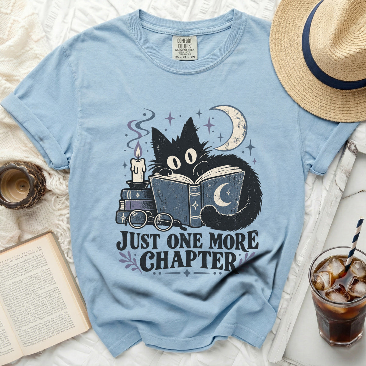 Light blue t-shirt with black cat reading and "Just One More Chapter" text.