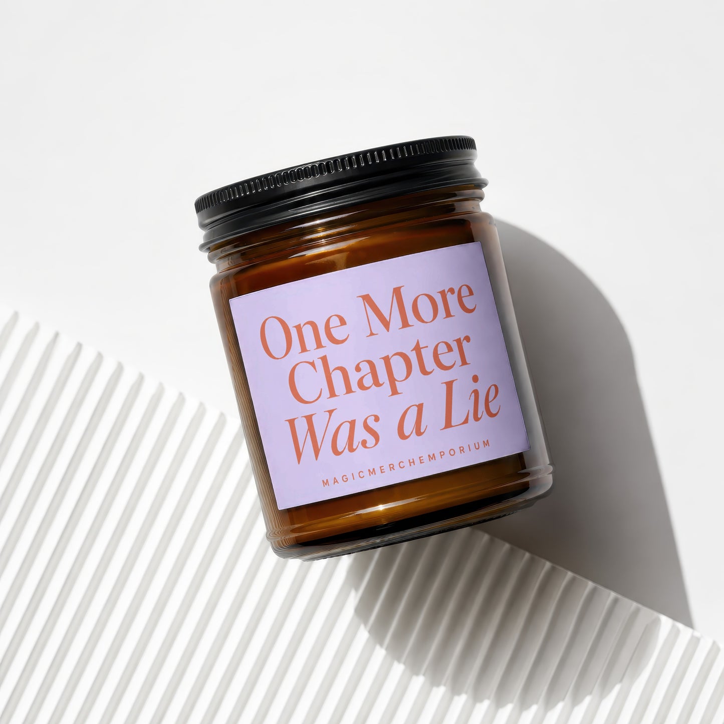 Amber jar candle with a light purple label that reads "One More Chapter Was a Lie".