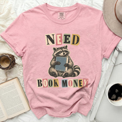 Pink t-shirt with raccoon holding book, text "NEED BOOK MONEY".