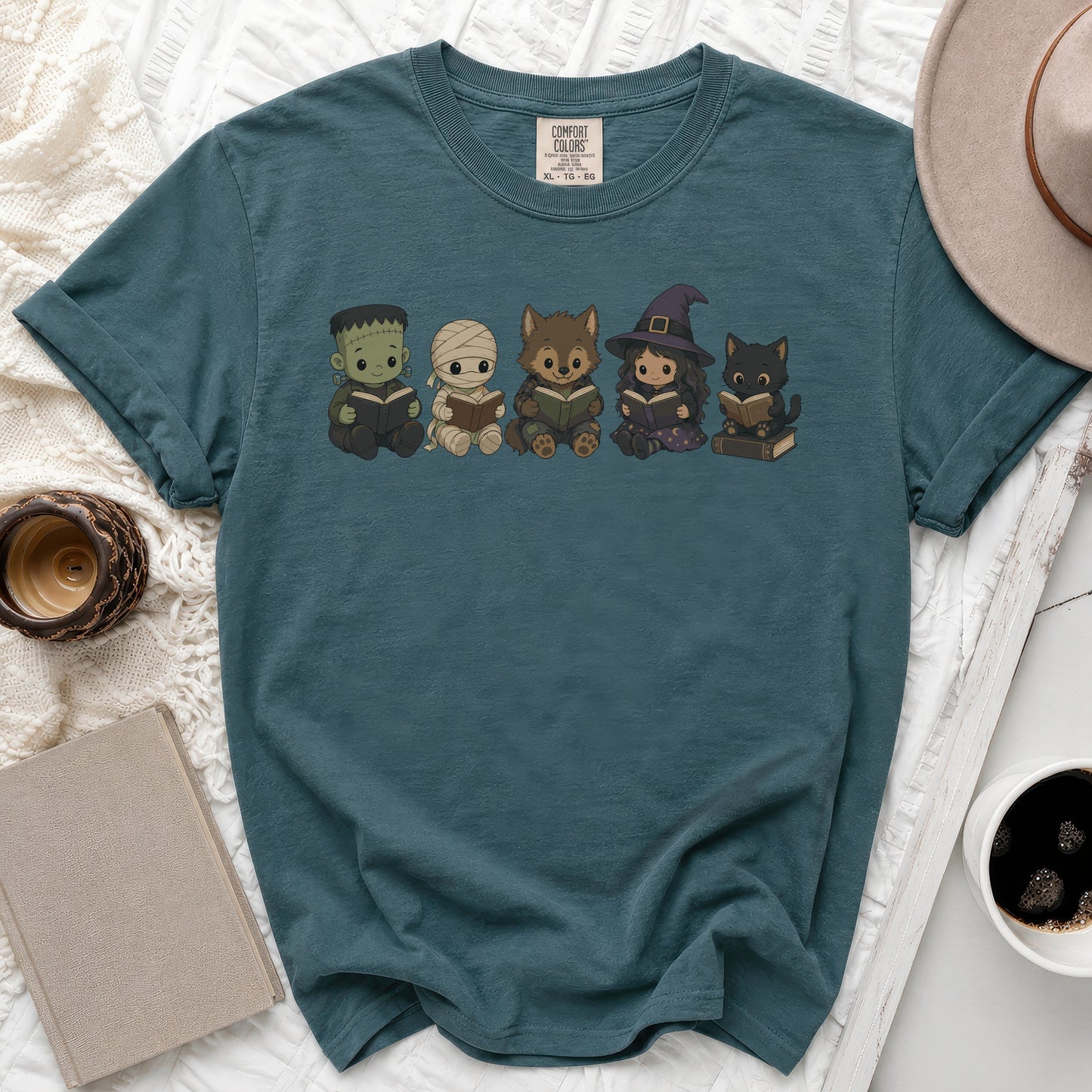 Teal t-shirt with cartoon style Frankenstein, mummy, werewolf, witch, and cat reading books.
