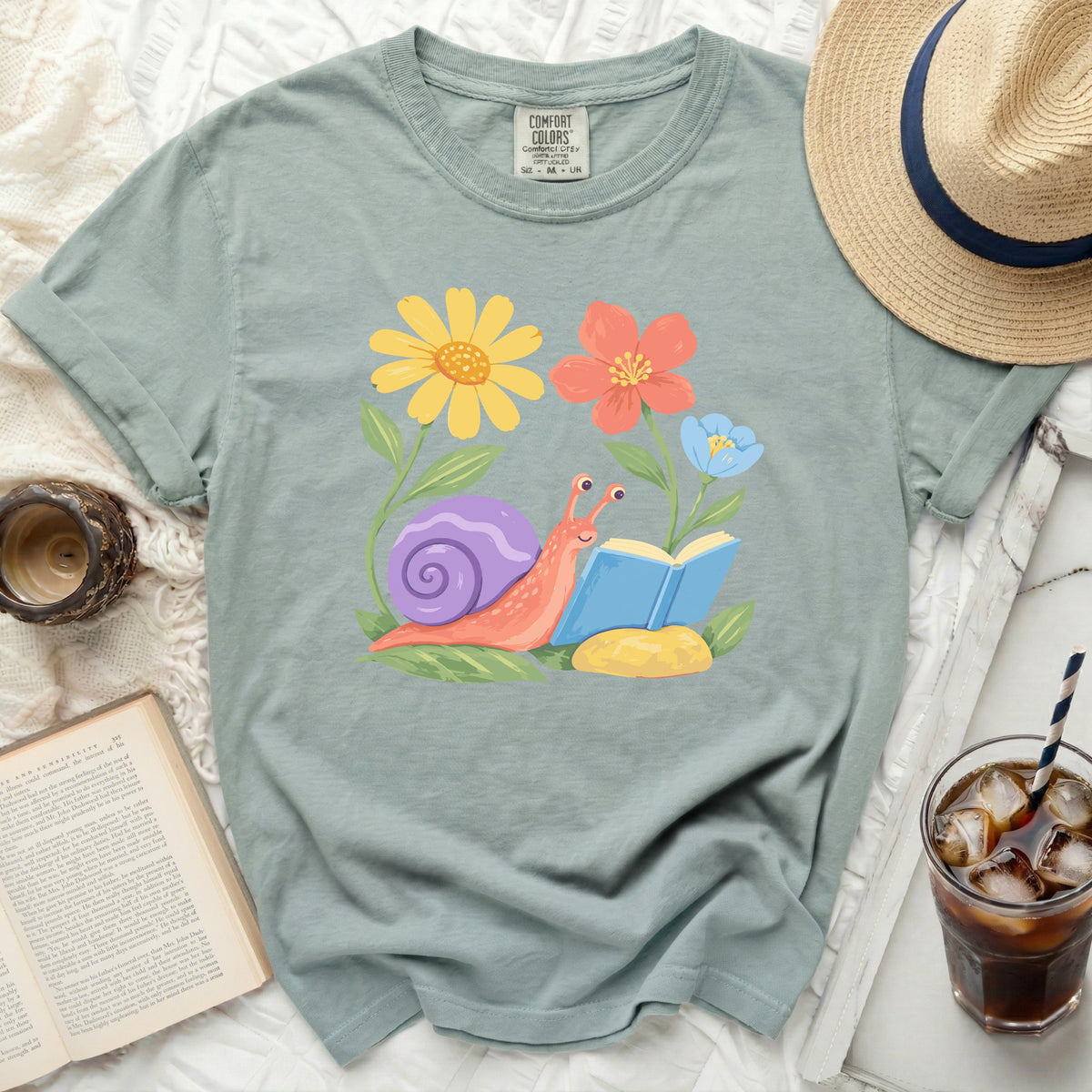 Green t-shirt with a cartoon snail reading a book among flowers.