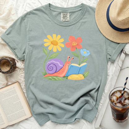 Green t-shirt with a cartoon snail reading a book among flowers.