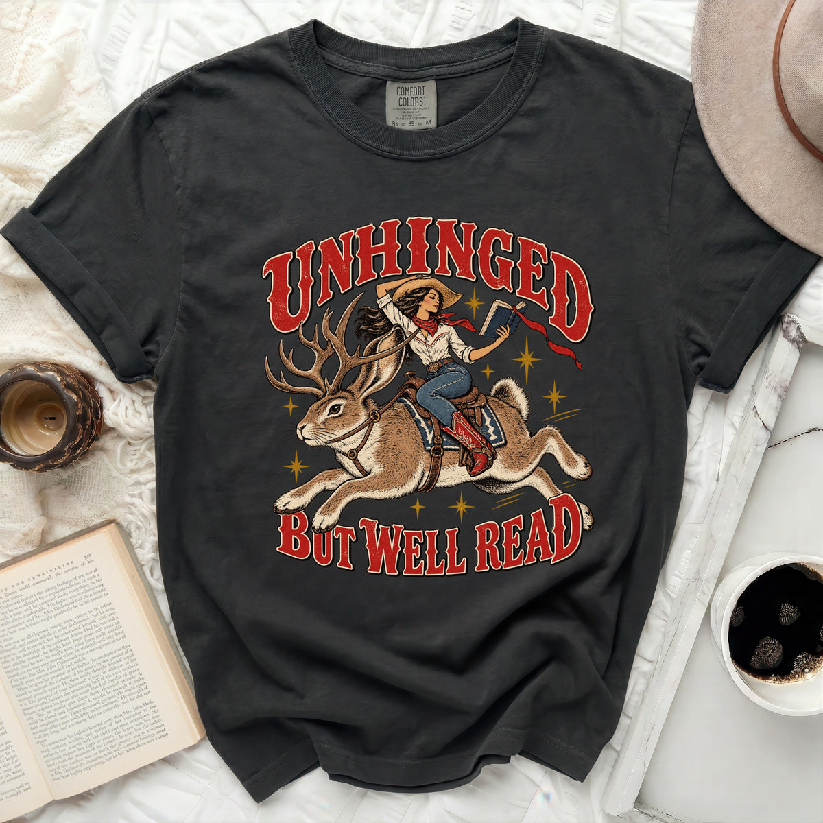 Black t-shirt with "Unhinged but well read" text and graphic of woman riding jackalope.