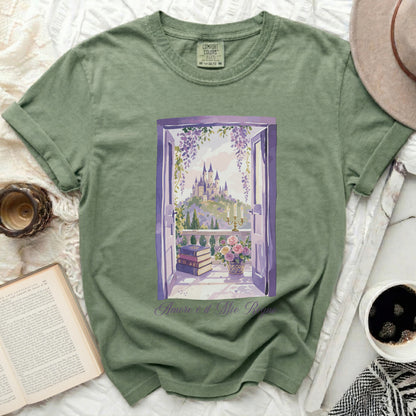 Green t-shirt with illustration of a castle viewed through an open window, with books and flowers.